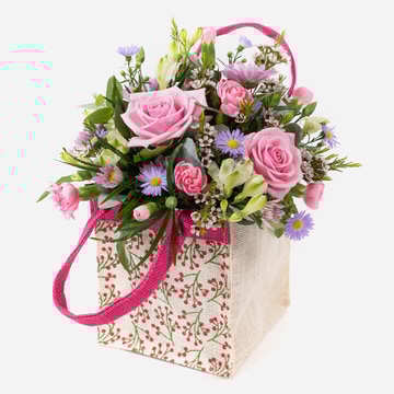 A little something pink floral arrangement in a jute gift bag with roses and carnations