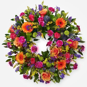 Bright circular funeral wreath with mixed gerberas roses and carnations in vibrant colours