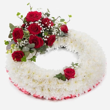 White funeral wreath with red roses and red ribbon edging