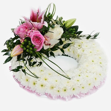 Pink massed wreath made with white chrysanthemum and a pink rose and lily feature on a grey background