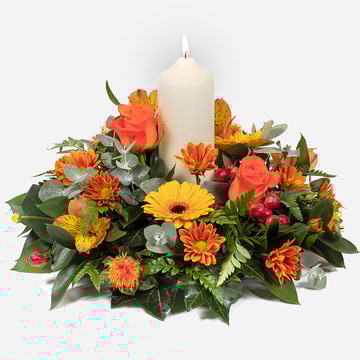 Warm glow an autumn centerpiece with orange roses yellow gerberas and a central candle