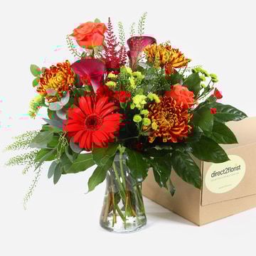 Fiery horizon bouquet with red gerberas orange roses and seasonal flowers in kraft wrap beside direct2florist delivery box