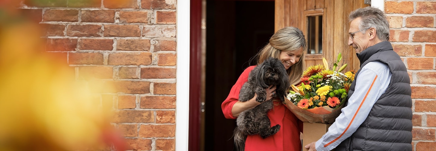 Woman with dog receiving autumn flower bouquet at her door.