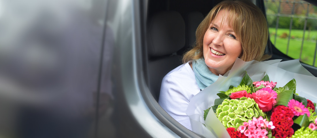 Smiling woman receiving a surprise flower delivery at her front door from a local florist