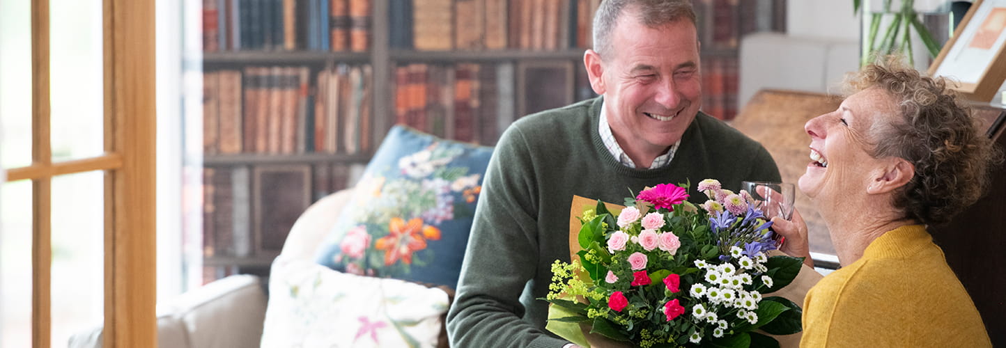 Man giving a colourful bouquet to a smiling woman at home