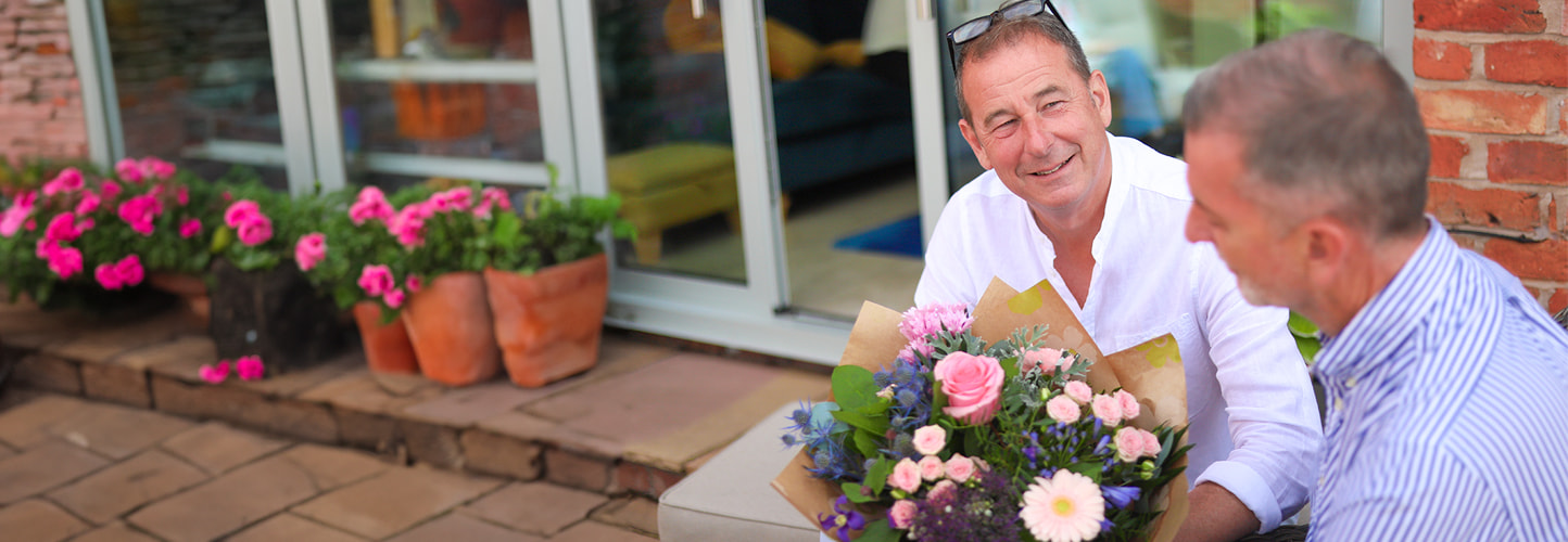 Man surprising a friend with a fresh bouquet while sitting outside a home
