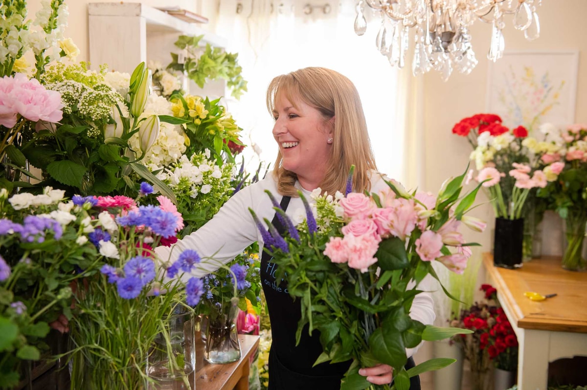 Happy florist wearing apron selecting stems surrounded by vibrant flowers