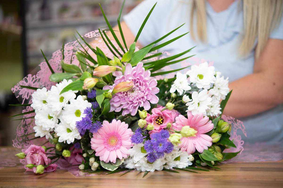 Close of a mixed bouquet in pink, white and purple being made on a table
