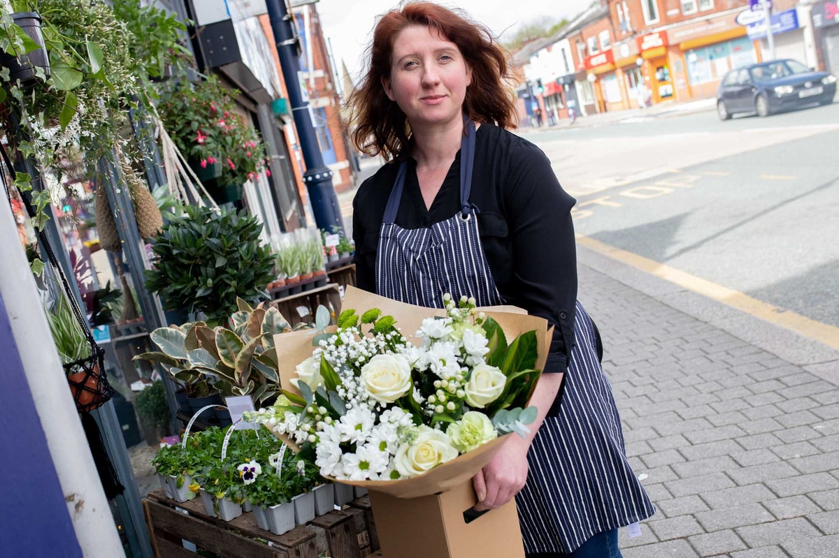 Florist in a striped apron outside a flowershop holding a cream themed boxed hand-tied.