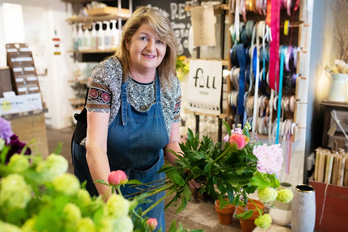 Florist in flowershop holding a stem whilst leaning down and choosing more flowers.