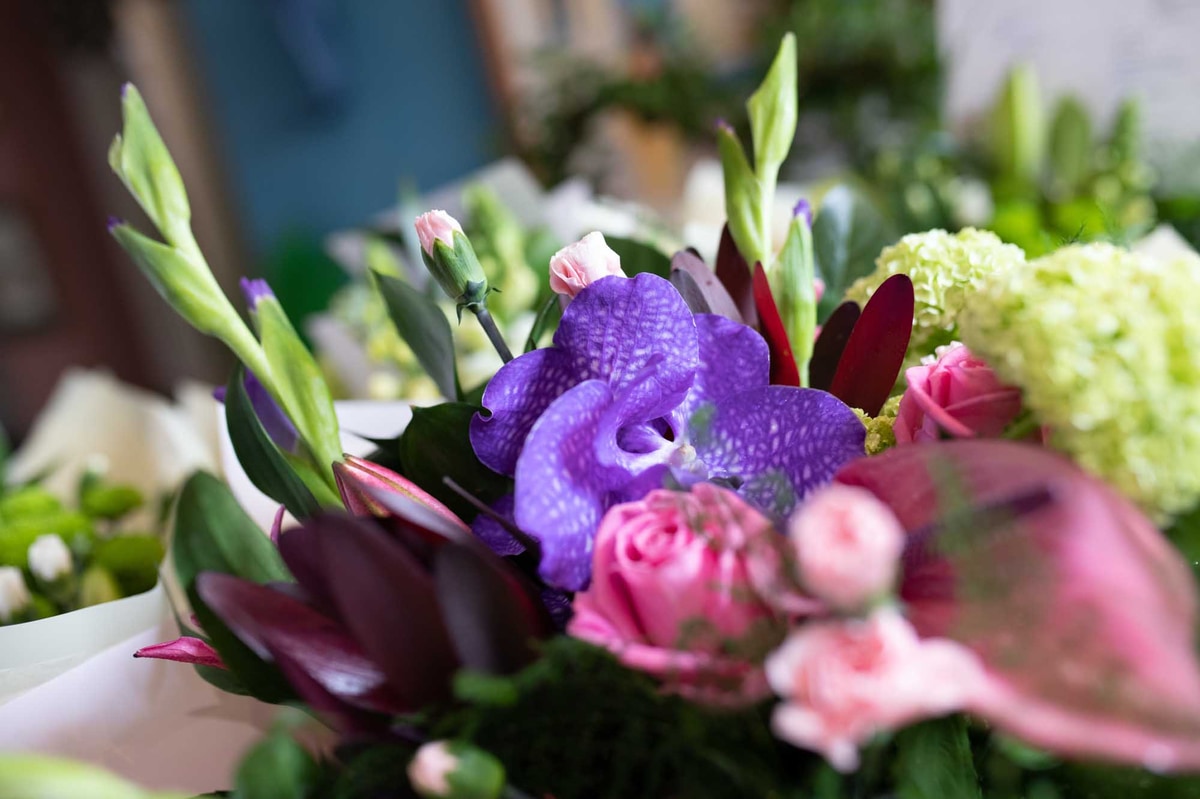 Close-up of a vibrant floral arrangement with purple orchids, pink roses, and assorted greenery in soft, natural lighting.