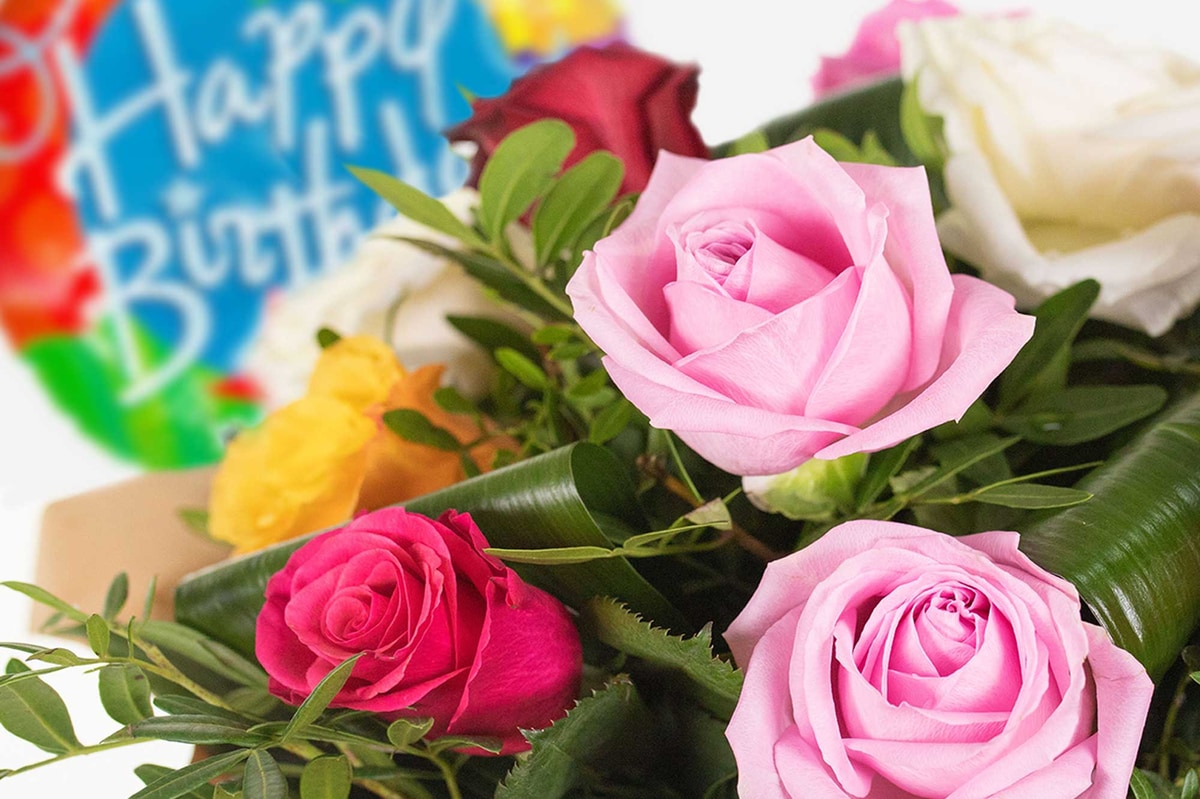 Close-up of a multi-coloured rose bouquet with happy birthday balloon in the background