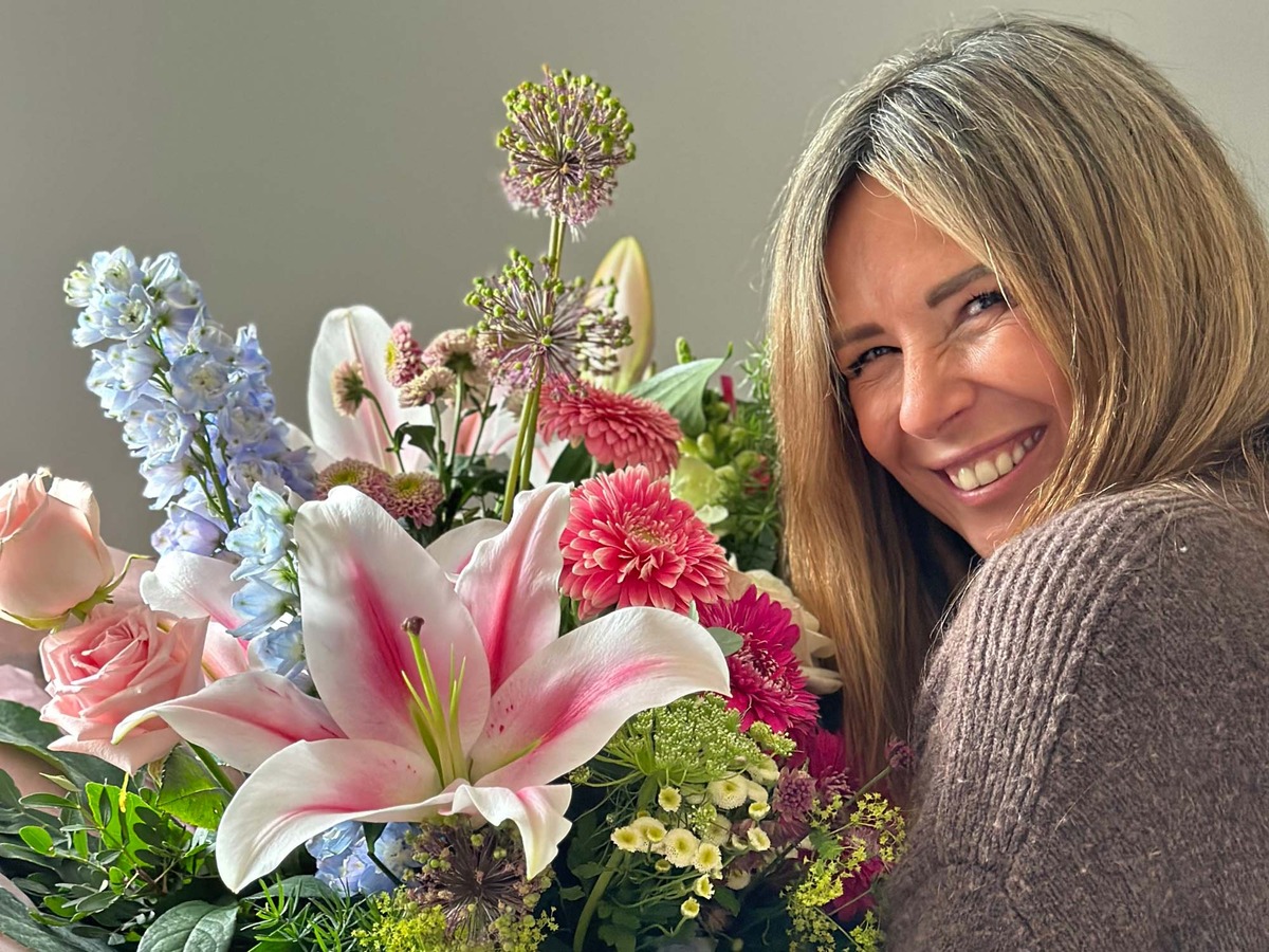 Close-up of smiling woman in a brown cardigan holding a vibrant luxury arrangement featuring pink oriental lilies