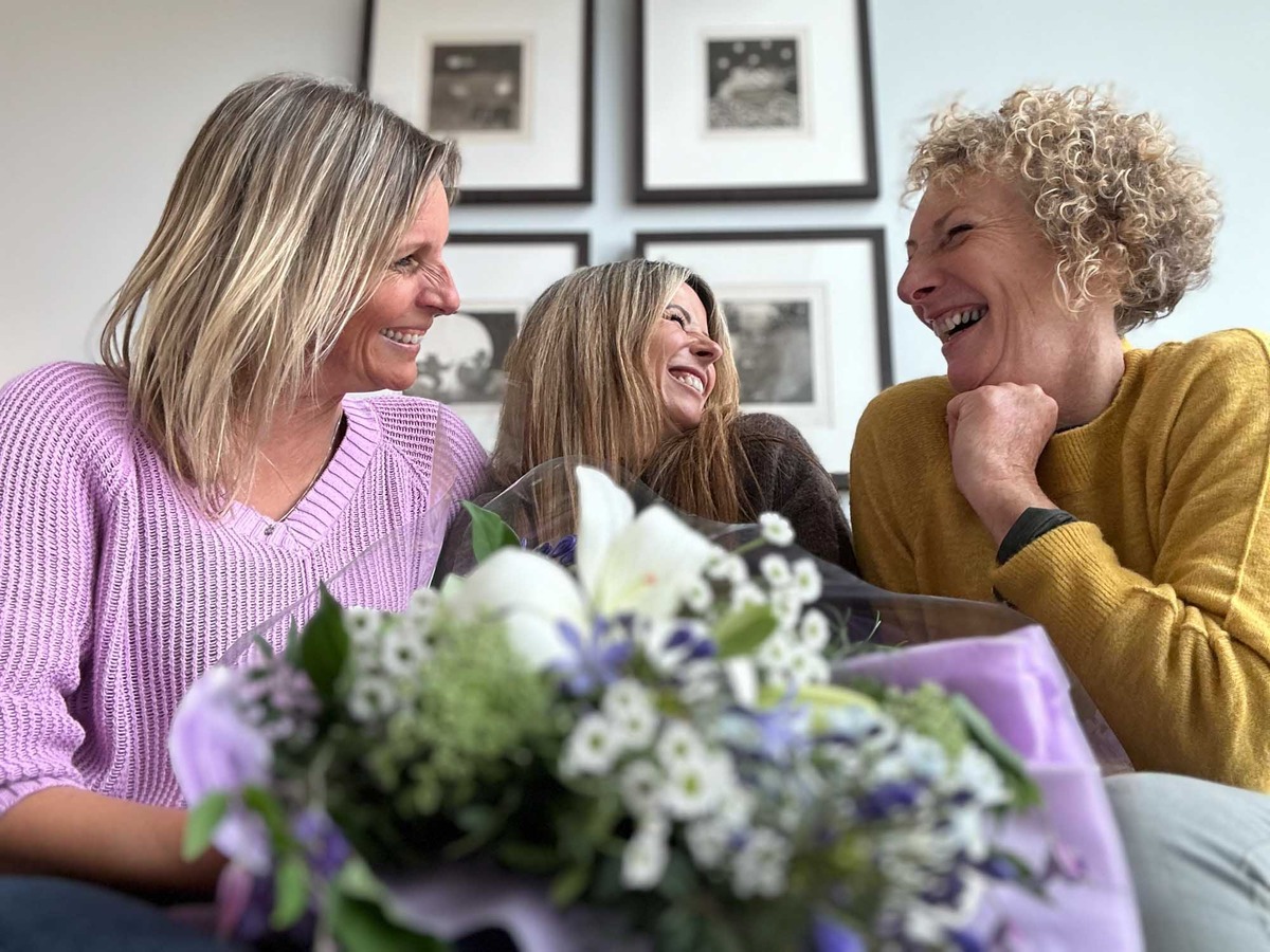 3 happy women friends enjoying each others company, laughing with a purple wrap of flowers featuring
