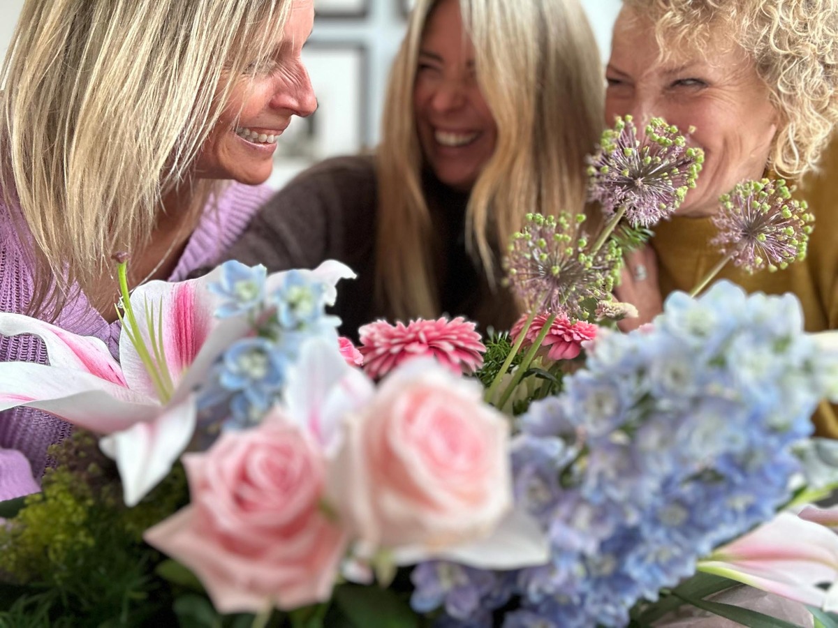 Group of 3 woman in a happy conversation with a bokeh of a pastel themed arrangement in the foreground.